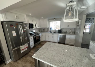 Bright modern kitchen with white cabinets, stainless steel appliances, granite island, and large window overlooking the outdoors.