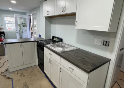 Modern kitchen with white cabinetry and dark wood countertop, featuring a black stove and unfinished flooring, waiting for final touches