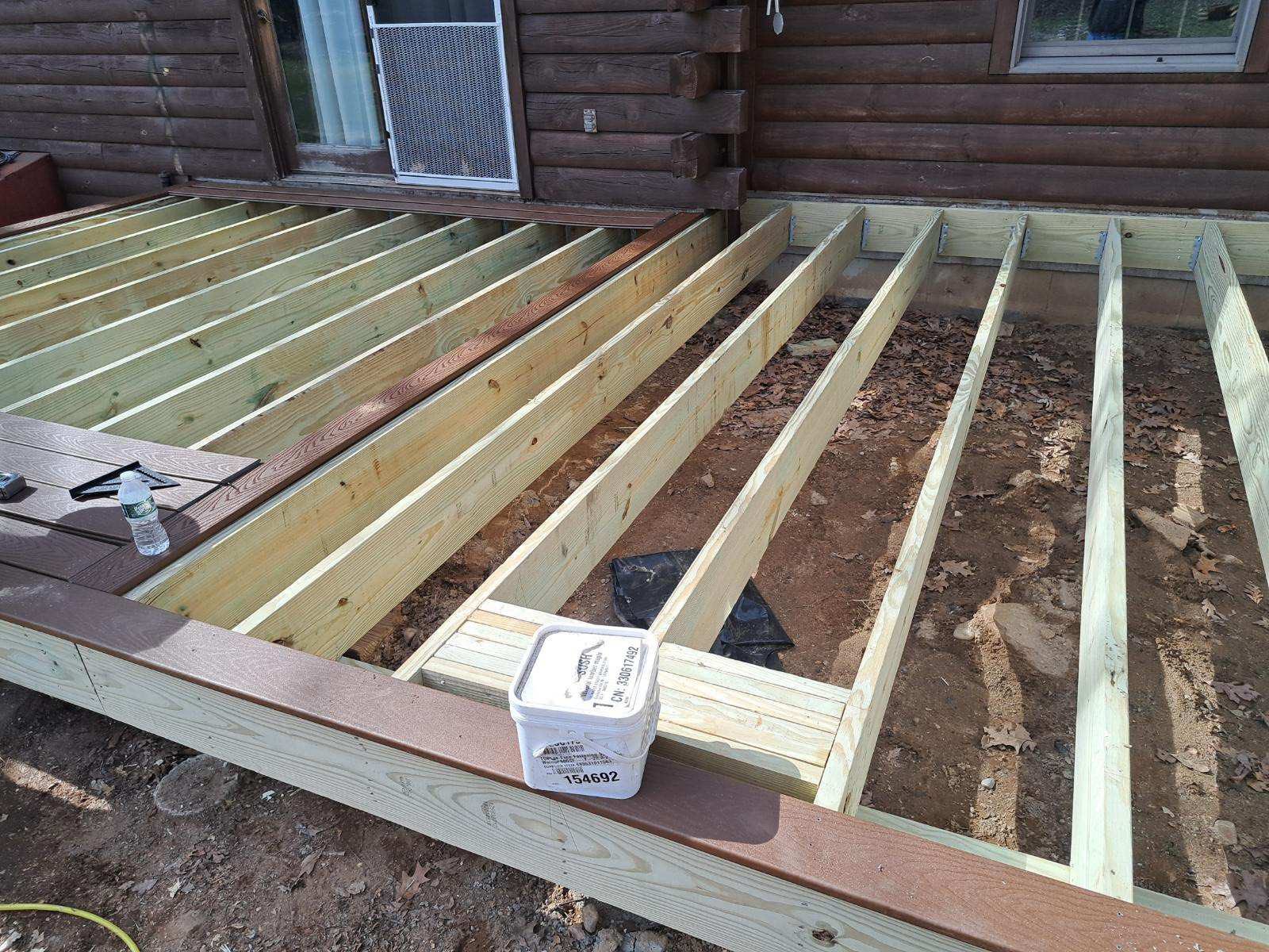 In-progress deck construction showing pressure-treated wood framing and composite decking installation at a log cabin home in Andover, CT project by Lagace Construction.